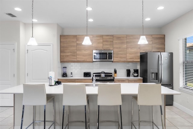 kitchen featuring visible vents, a breakfast bar area, appliances with stainless steel finishes, light countertops, and backsplash