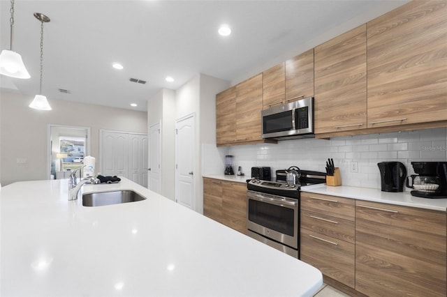 kitchen featuring brown cabinets, visible vents, decorative backsplash, appliances with stainless steel finishes, and a sink