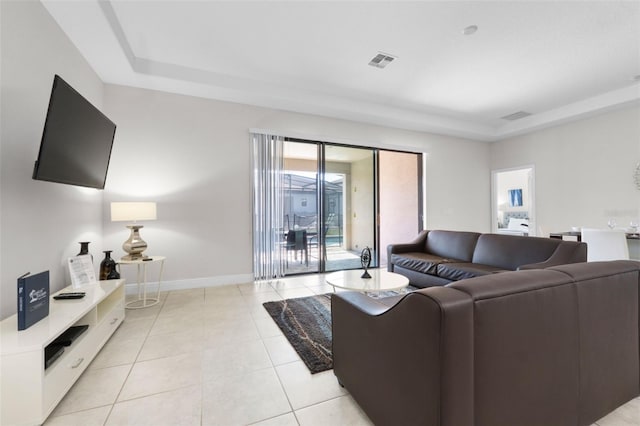 living area featuring light tile patterned floors, a tray ceiling, visible vents, and baseboards