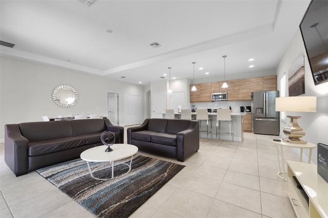 living area featuring a tray ceiling, light tile patterned flooring, visible vents, and recessed lighting