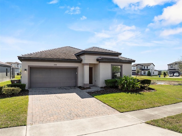 prairie-style home with a garage, decorative driveway, a front lawn, and stucco siding