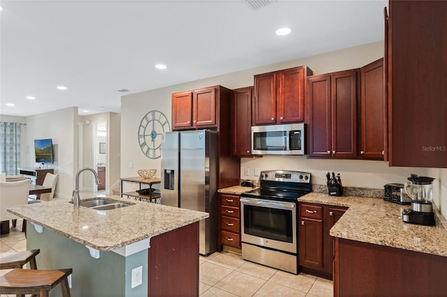 kitchen featuring light stone countertops, an island with sink, appliances with stainless steel finishes, and sink