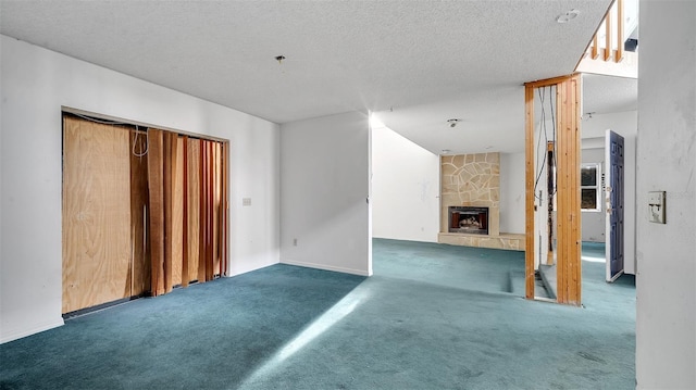 unfurnished living room featuring a stone fireplace, a textured ceiling, and dark colored carpet