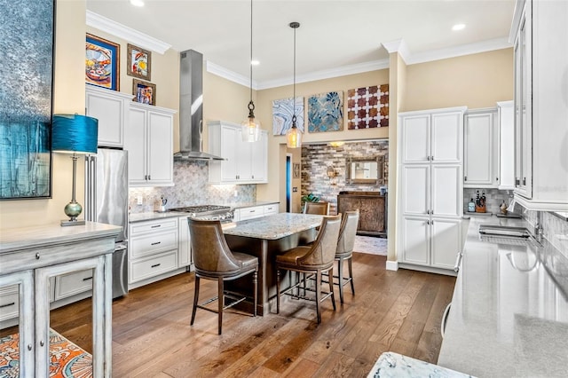 kitchen featuring pendant lighting, white cabinets, a breakfast bar, and wall chimney range hood