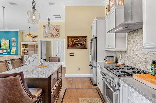 kitchen featuring decorative light fixtures, high quality appliances, a breakfast bar area, white cabinets, and wall chimney exhaust hood