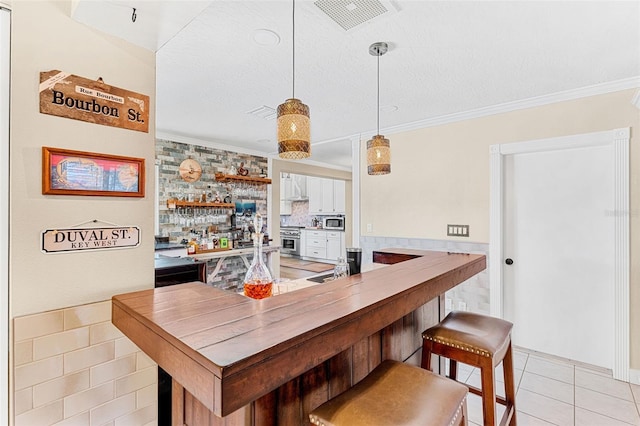 bar featuring crown molding, appliances with stainless steel finishes, hanging light fixtures, white cabinets, and light tile patterned flooring