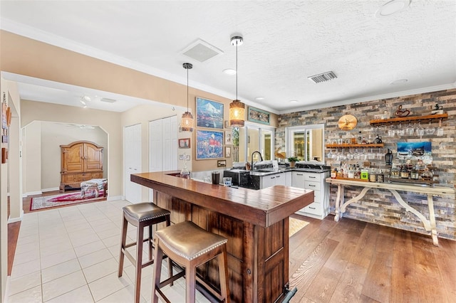 kitchen featuring white cabinetry, crown molding, a textured ceiling, kitchen peninsula, and pendant lighting