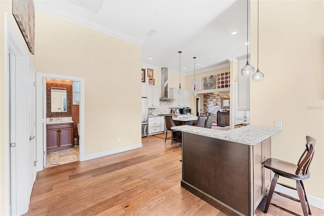 kitchen featuring pendant lighting, stainless steel fridge, white cabinetry, a kitchen breakfast bar, and wall chimney exhaust hood