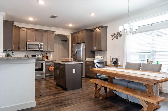 kitchen featuring appliances with stainless steel finishes, decorative light fixtures, dark wood-type flooring, crown molding, and dark brown cabinets