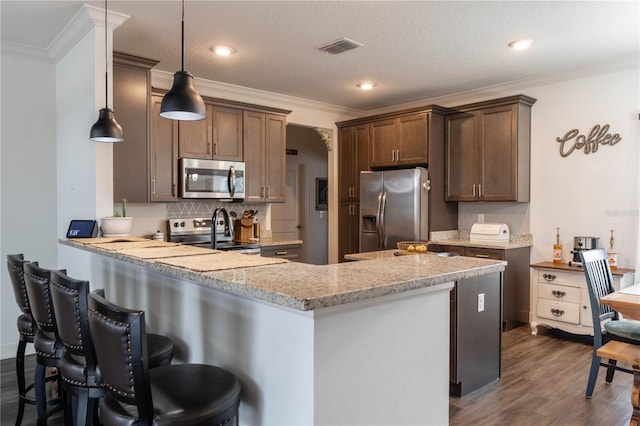 kitchen with appliances with stainless steel finishes, hanging light fixtures, a kitchen breakfast bar, light stone countertops, and kitchen peninsula