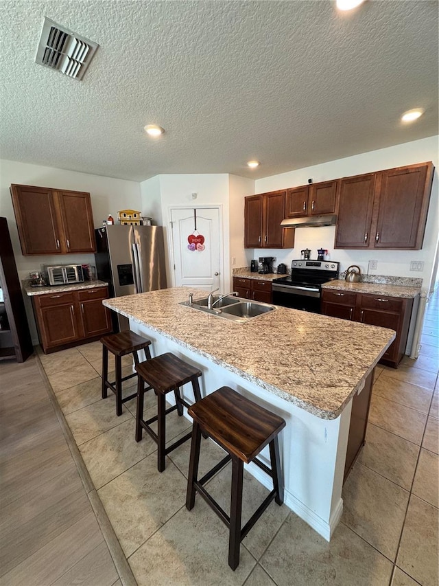 kitchen featuring sink, stainless steel appliances, a kitchen breakfast bar, light stone countertops, and a center island with sink