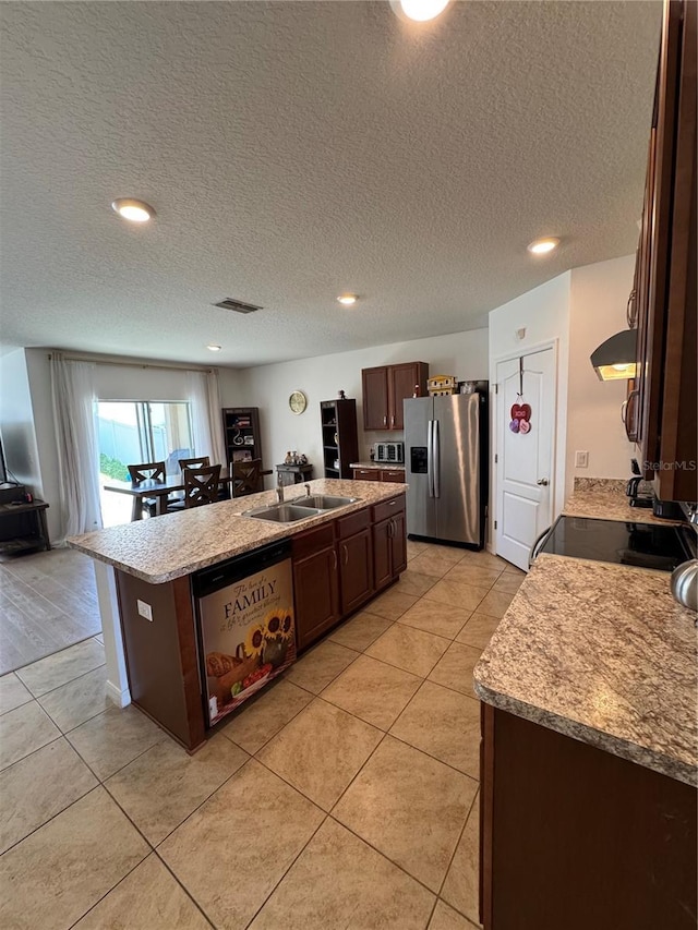 kitchen featuring sink, light tile patterned floors, light stone counters, stainless steel appliances, and a center island with sink