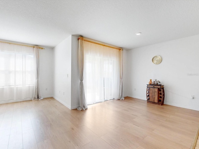 empty room with baseboards, light wood-style flooring, and a textured ceiling