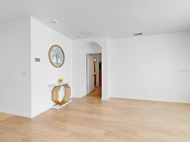 unfurnished room featuring light wood-style floors, arched walkways, visible vents, and a textured ceiling