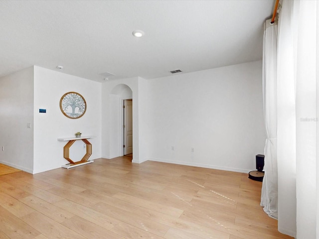 spare room featuring arched walkways, baseboards, visible vents, and light wood finished floors