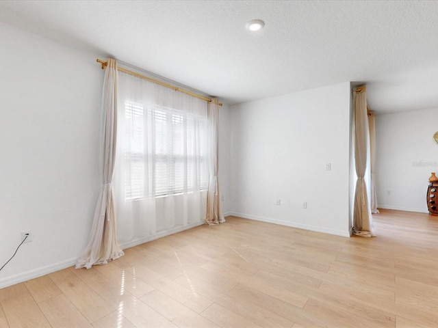 spare room featuring a textured ceiling, baseboards, and light wood-style floors