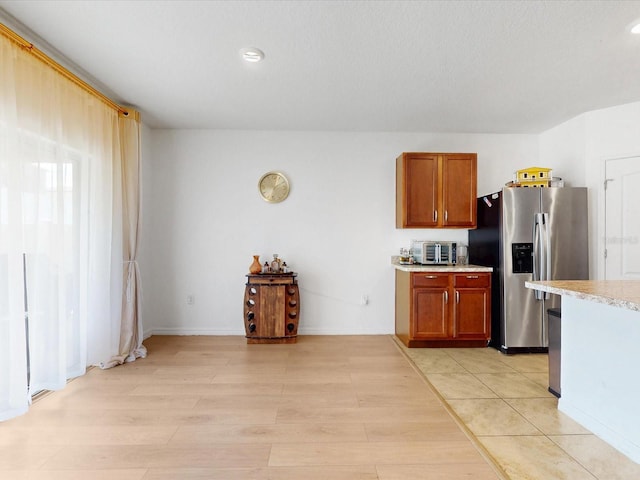 kitchen featuring brown cabinetry, light countertops, light wood finished floors, and stainless steel fridge with ice dispenser