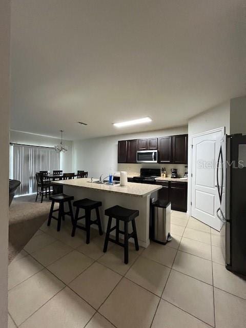 kitchen with a breakfast bar, a kitchen island with sink, dark brown cabinetry, black appliances, and decorative light fixtures