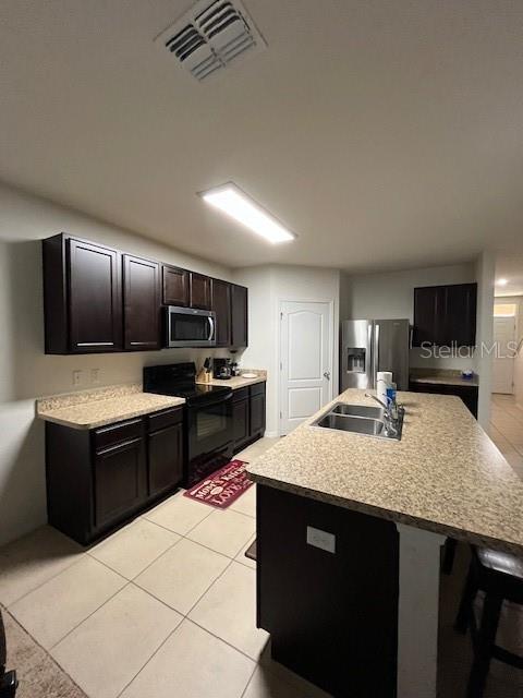 kitchen featuring appliances with stainless steel finishes, an island with sink, sink, light tile patterned floors, and dark brown cabinetry