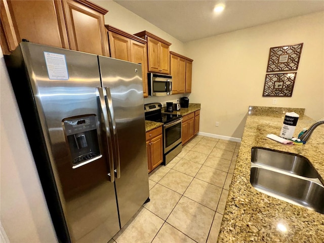 kitchen with brown cabinets, a sink, stainless steel appliances, light tile patterned floors, and light stone countertops