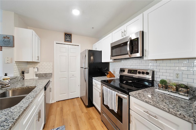 kitchen with appliances with stainless steel finishes, sink, white cabinetry, and light stone counters