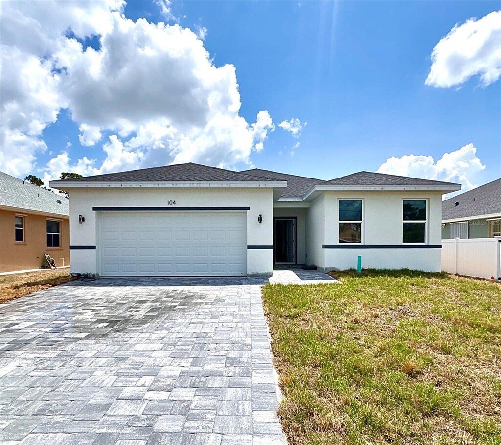 104 Australian Dr, Rotonda West, FL 33947 - view of front of home with a garage, decorative driveway, stucco siding, and fence