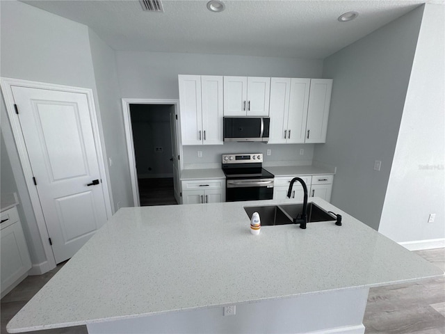 104 Australian Dr, Rotonda West, FL 33947 - kitchen featuring appliances with stainless steel finishes, light stone counters, white cabinetry, a center island with sink, and a textured ceiling