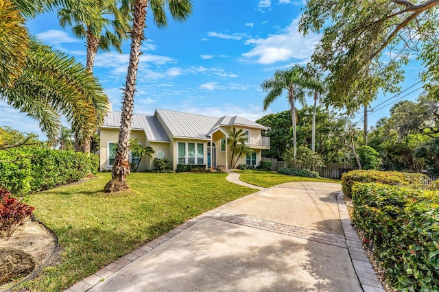 view of front of house featuring stucco siding, fence, concrete driveway, a front yard, and metal roof