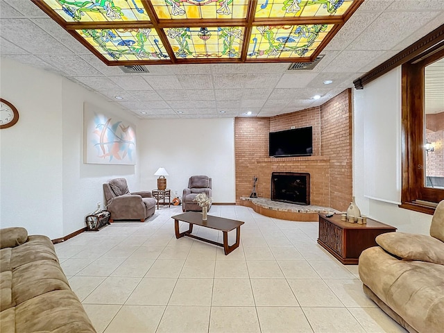 living room featuring a brick fireplace, light tile patterned floors, and a drop ceiling