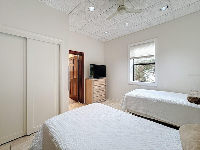 tiled bedroom with ceiling fan, a closet, and a drop ceiling