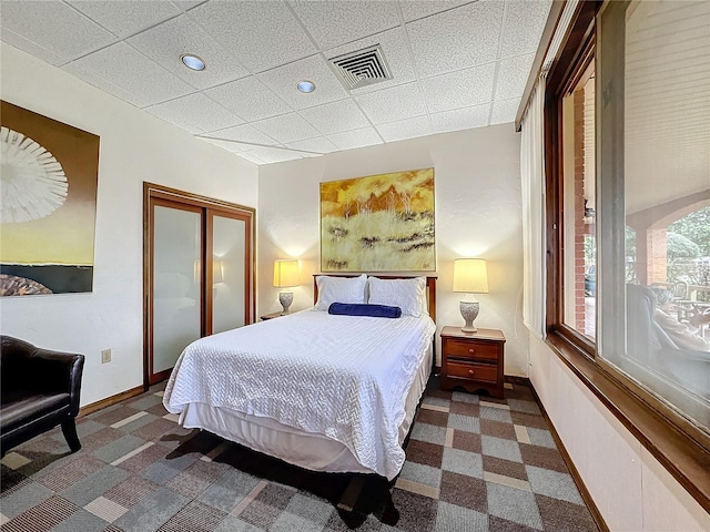 carpeted bedroom with a paneled ceiling and a closet