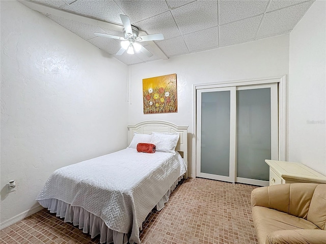 bedroom with a drop ceiling, ceiling fan, and a closet