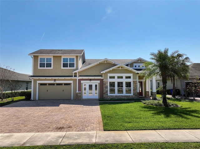 craftsman house with a garage, stone siding, decorative driveway, french doors, and a front yard