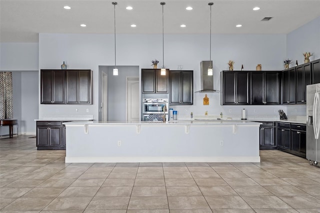 kitchen featuring stainless steel appliances, light countertops, visible vents, a high ceiling, and wall chimney range hood