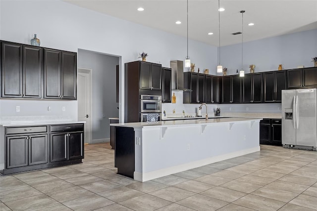 kitchen featuring a towering ceiling, wall chimney exhaust hood, a breakfast bar area, light countertops, and stainless steel refrigerator with ice dispenser