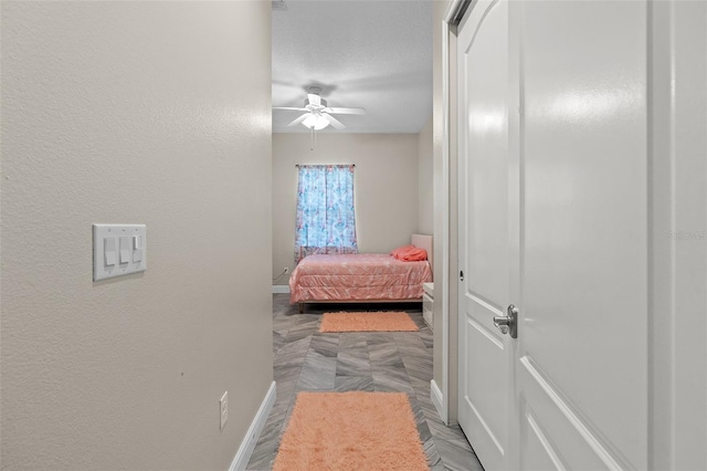 bedroom with ceiling fan, baseboards, a textured ceiling, and a textured wall