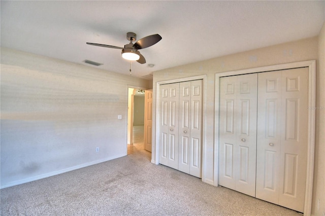 unfurnished bedroom featuring light carpet, two closets, and ceiling fan