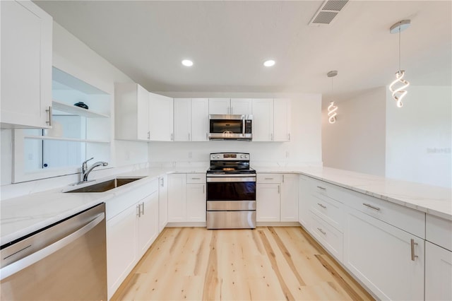 kitchen with pendant lighting, white cabinetry, sink, stainless steel appliances, and light stone countertops