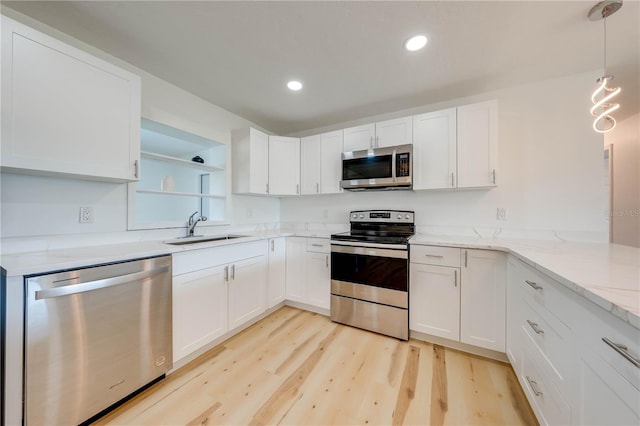 kitchen with sink, white cabinetry, stainless steel appliances, light stone countertops, and decorative light fixtures