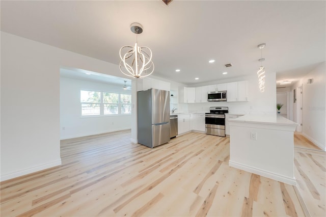 kitchen with hanging light fixtures, kitchen peninsula, stainless steel appliances, light hardwood / wood-style floors, and white cabinets