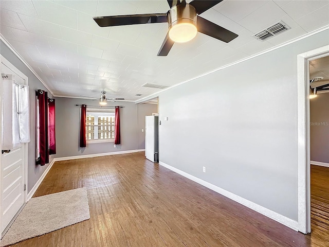 empty room featuring visible vents, ornamental molding, ceiling fan, wood finished floors, and baseboards