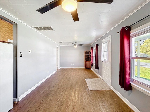 empty room with crown molding, wood finished floors, visible vents, and a ceiling fan