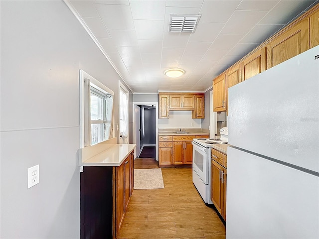 kitchen with light wood finished floors, light countertops, visible vents, a sink, and white appliances