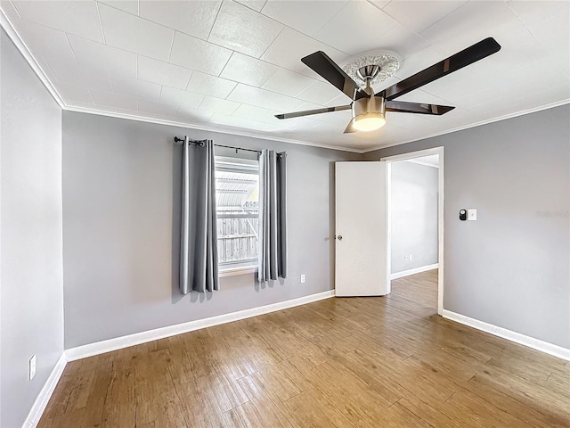 spare room featuring crown molding, baseboards, ceiling fan, and wood finished floors