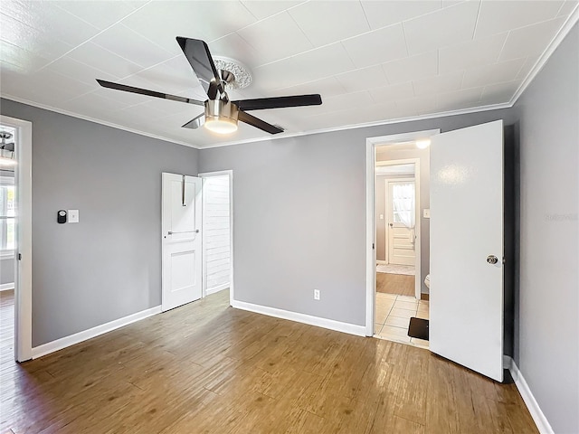 unfurnished bedroom with ensuite bathroom, ornamental molding, a ceiling fan, wood finished floors, and baseboards