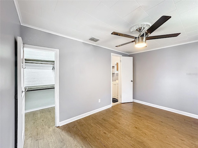 spare room featuring wood finished floors, visible vents, a ceiling fan, baseboards, and ornamental molding