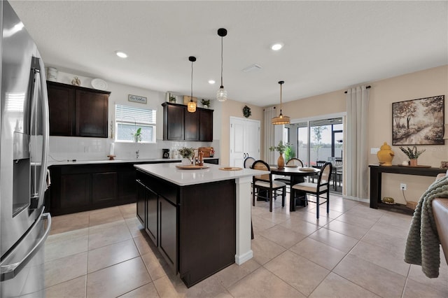 kitchen with hanging light fixtures, dark brown cabinets, stainless steel refrigerator with ice dispenser, a kitchen island, and decorative backsplash