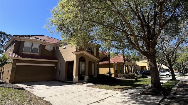 mediterranean / spanish home with a garage, a tiled roof, concrete driveway, and stucco siding