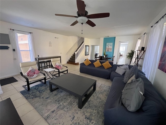 living area with ceiling fan, stairway, and light tile patterned flooring