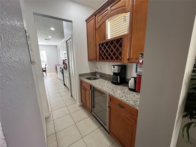 kitchen with beverage cooler, light tile patterned floors, brown cabinets, and light stone countertops